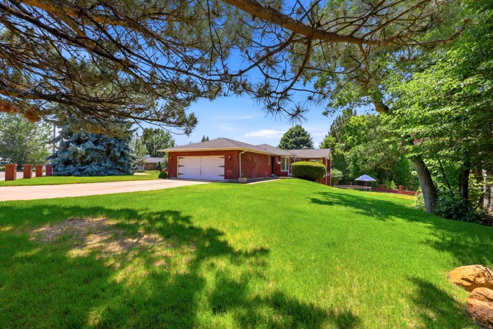 Expansive front yard featuring a manicured lawn, mature trees, and a brick exterior home with an attached garage