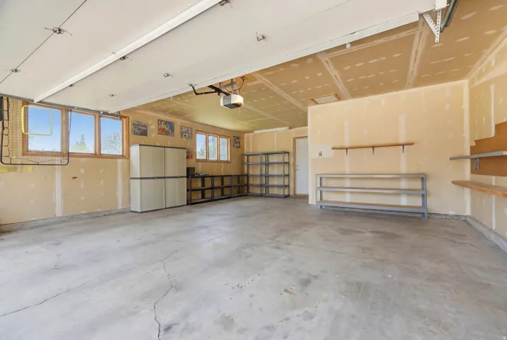 Spacious garage with multiple windows for natural light, concrete flooring, built-in shelving, and exposed ceiling joists