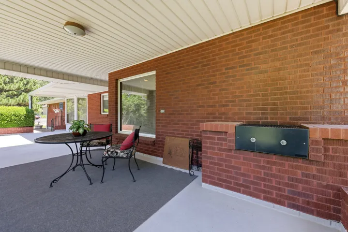 Covered patio featuring a slatted white ceiling, a built-in brick barbecue, an integrated outdoor grill, and expansive brick exterior walls