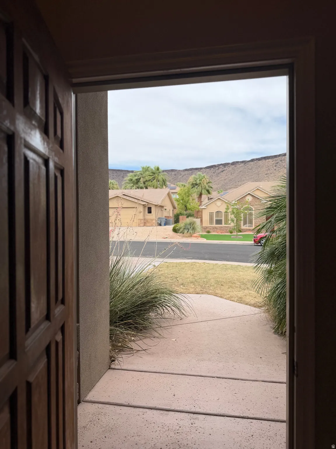Entryway with a paneled wood door opening to a concrete walkway and landscaped front yard