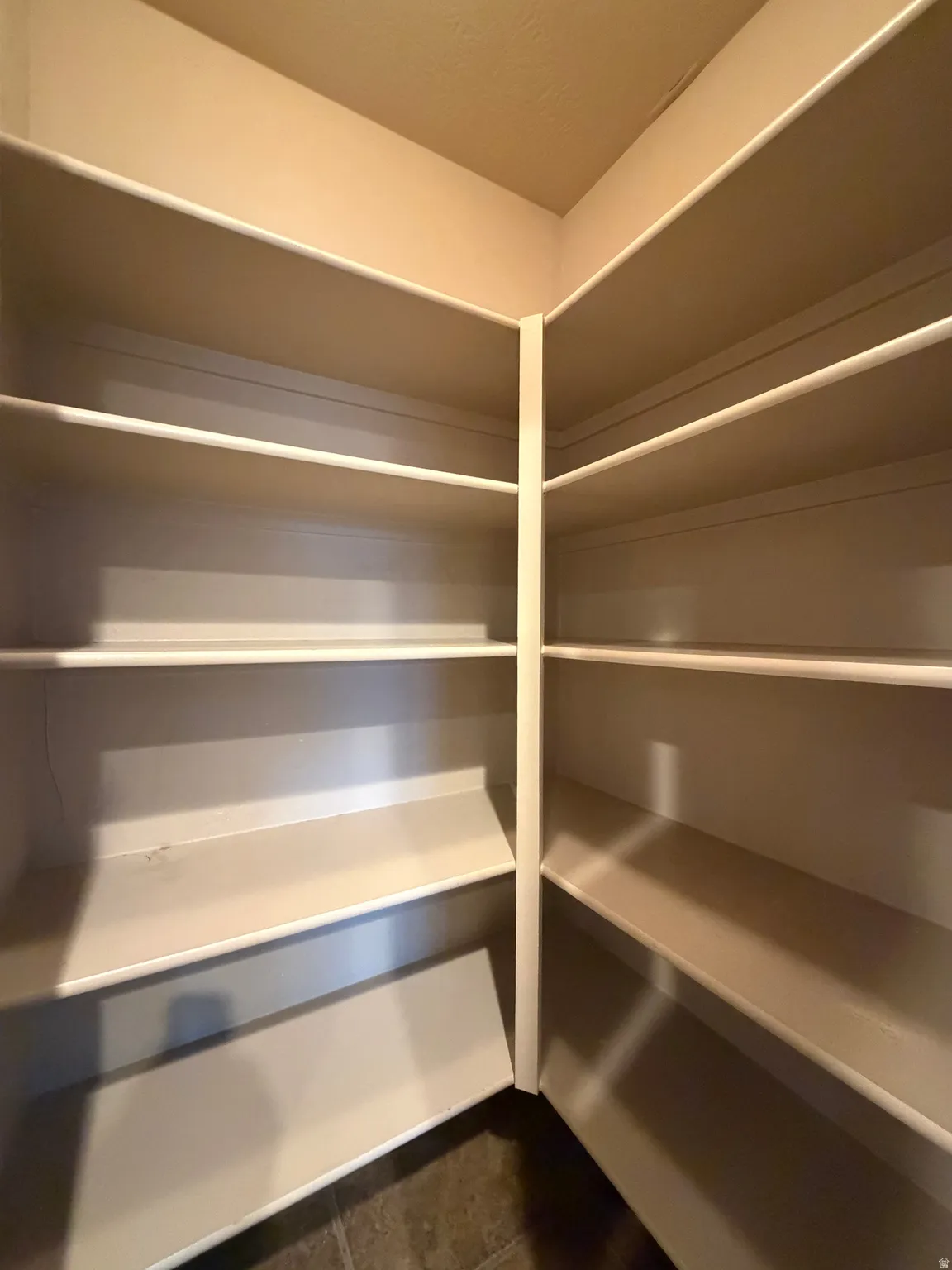 Corner pantry with multiple built-in shelves and dark tile flooring
