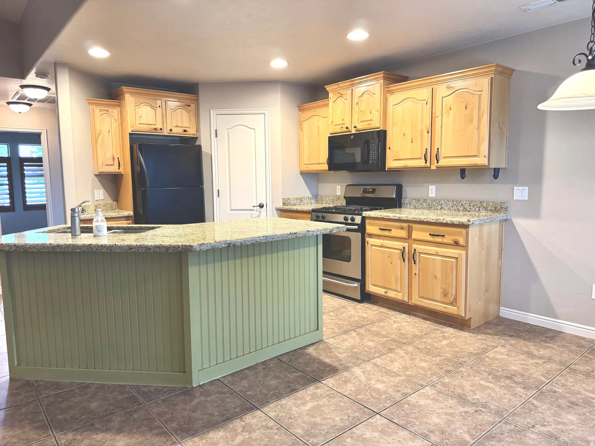 Kitchen featuring a peninsula with beadboard paneling, light-toned wood cabinetry, stone countertops, and tile flooring