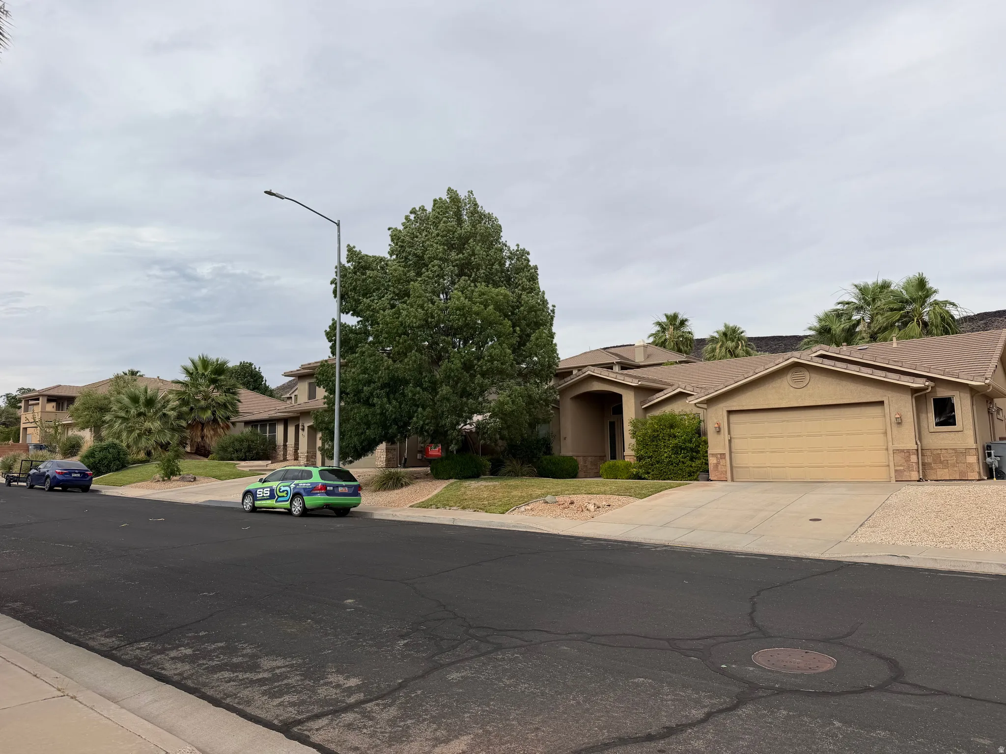 Stucco exterior home featuring a two-car garage, arched entry, and mature landscaping