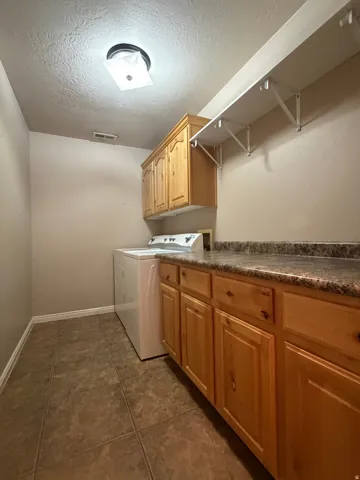 Utility room featuring wood cabinetry, a durable countertop, and tile flooring