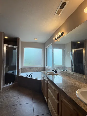 Bathroom featuring a corner soaking tub, a separate shower enclosure with a glass door, and a double vanity with built-in cabinetry