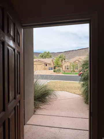 Entryway with a paneled wood door opening to a concrete walkway and landscaped front yard