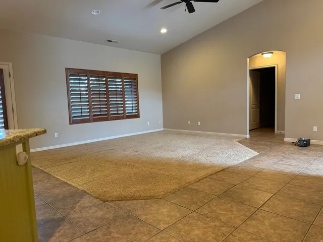Vaulted ceilings crown this spacious room, featuring a ceiling fan, recessed lighting, and a window with wood-finish shutters