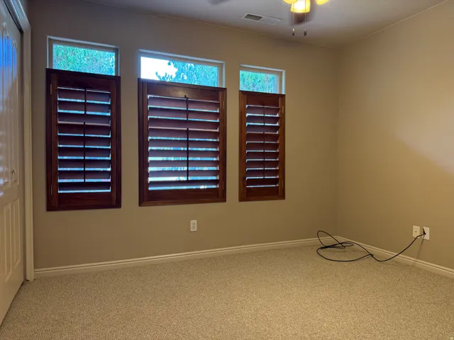 Three windows with wooden plantation shutters, complemented by neutral wall tones and textured carpeting