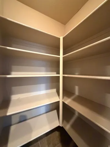Corner pantry with multiple built-in shelves and dark tile flooring