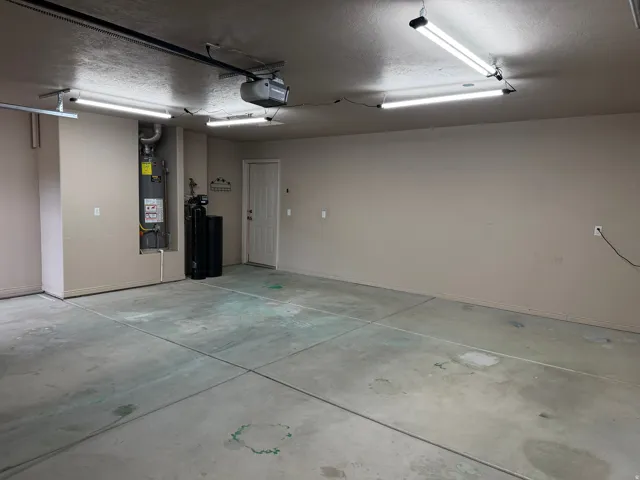 Spacious garage with concrete flooring, multiple overhead fluorescent light fixtures, and a white interior door