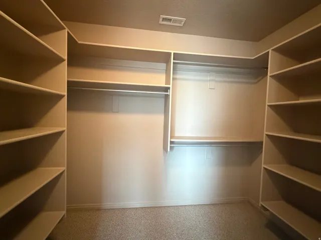 Walk-in closet featuring extensive built-in shelving, multiple hanging rods, and neutral-toned wall-to-wall carpeting