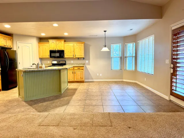 Open-concept living space with a kitchen island featuring beadboard paneling, light wood cabinetry, granite-finish countertops, and black appliances