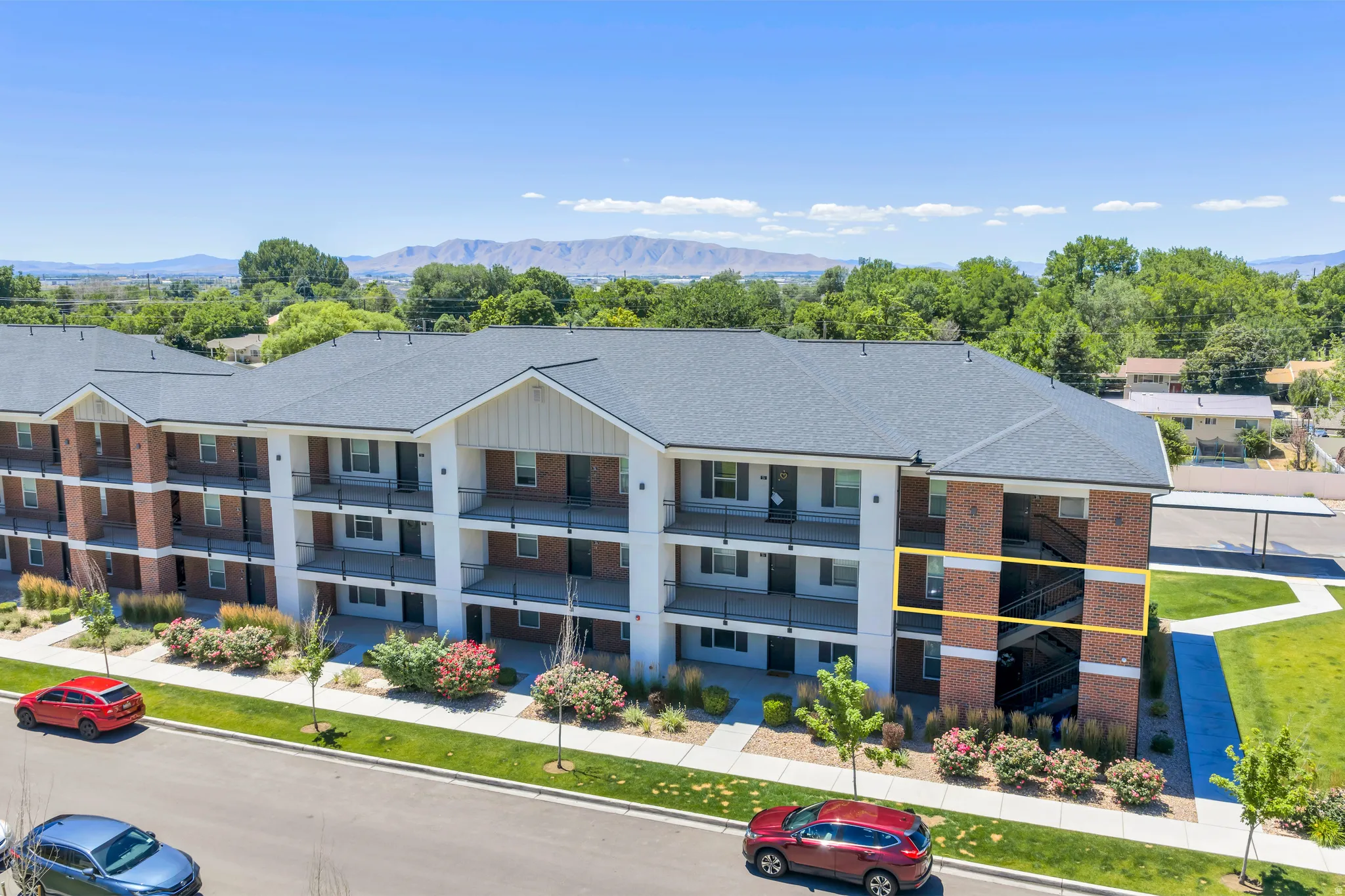 Multi-story residential building featuring brick and white siding, individual balconies, and a dark shingle roof