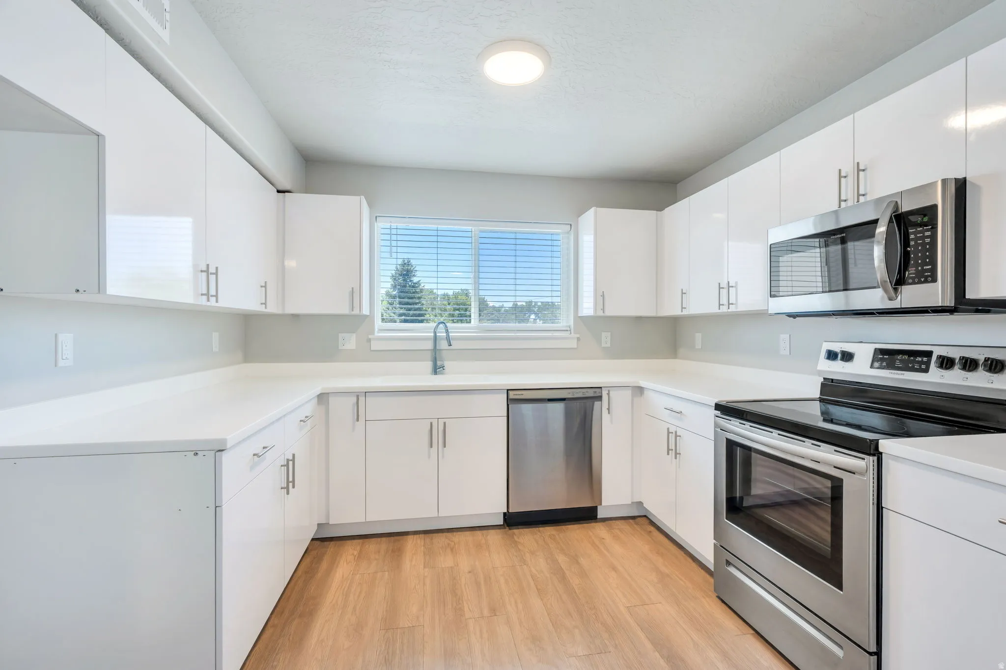 Contemporary kitchen featuring white cabinetry, light countertops, wood-finish flooring, a stainless steel electric range, and a built-in microwave