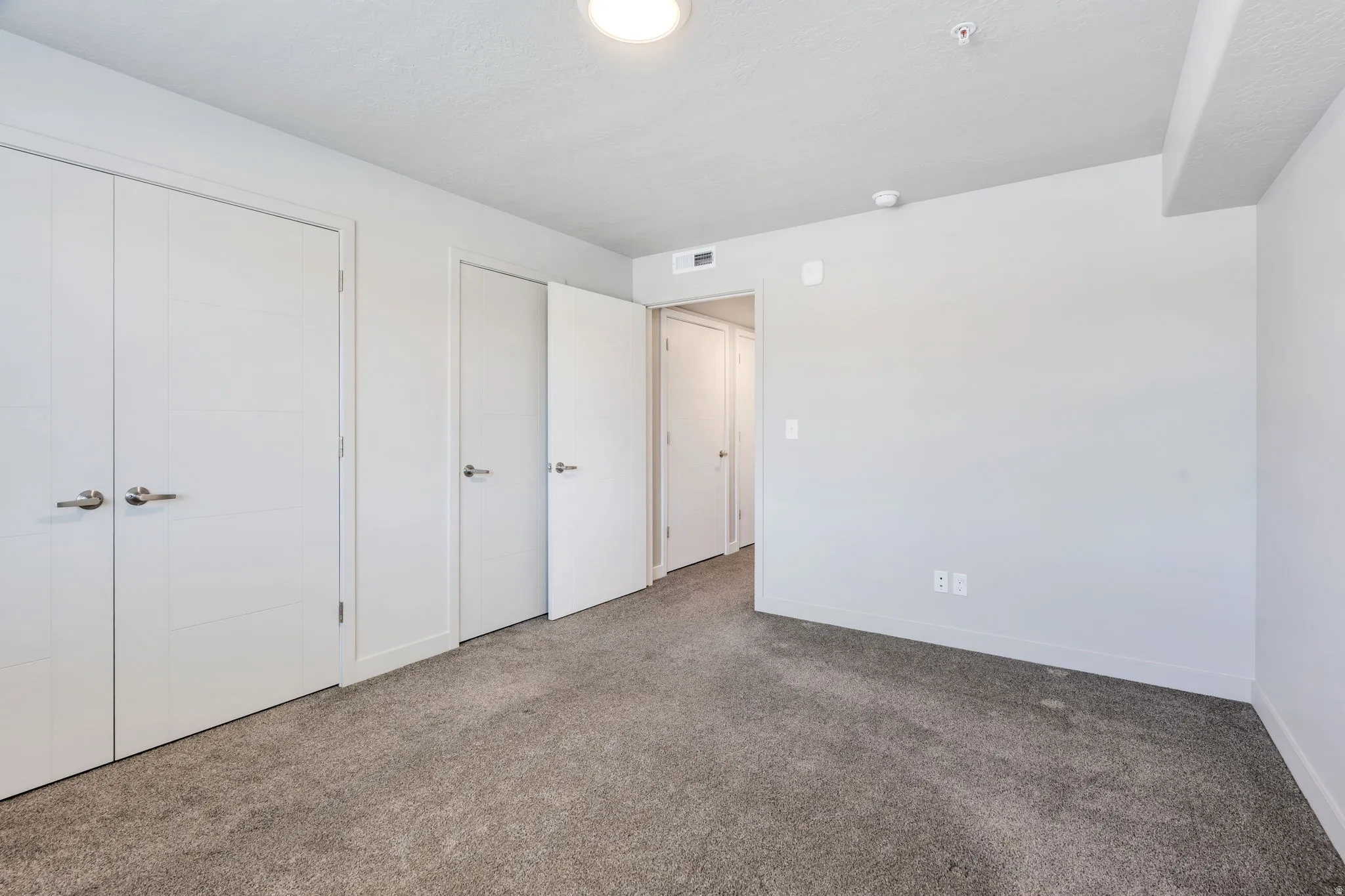 Neutral gray carpeting complementing light gray wall tones, recessed ceiling lighting, and multiple white panel doors with brushed nickel hardware