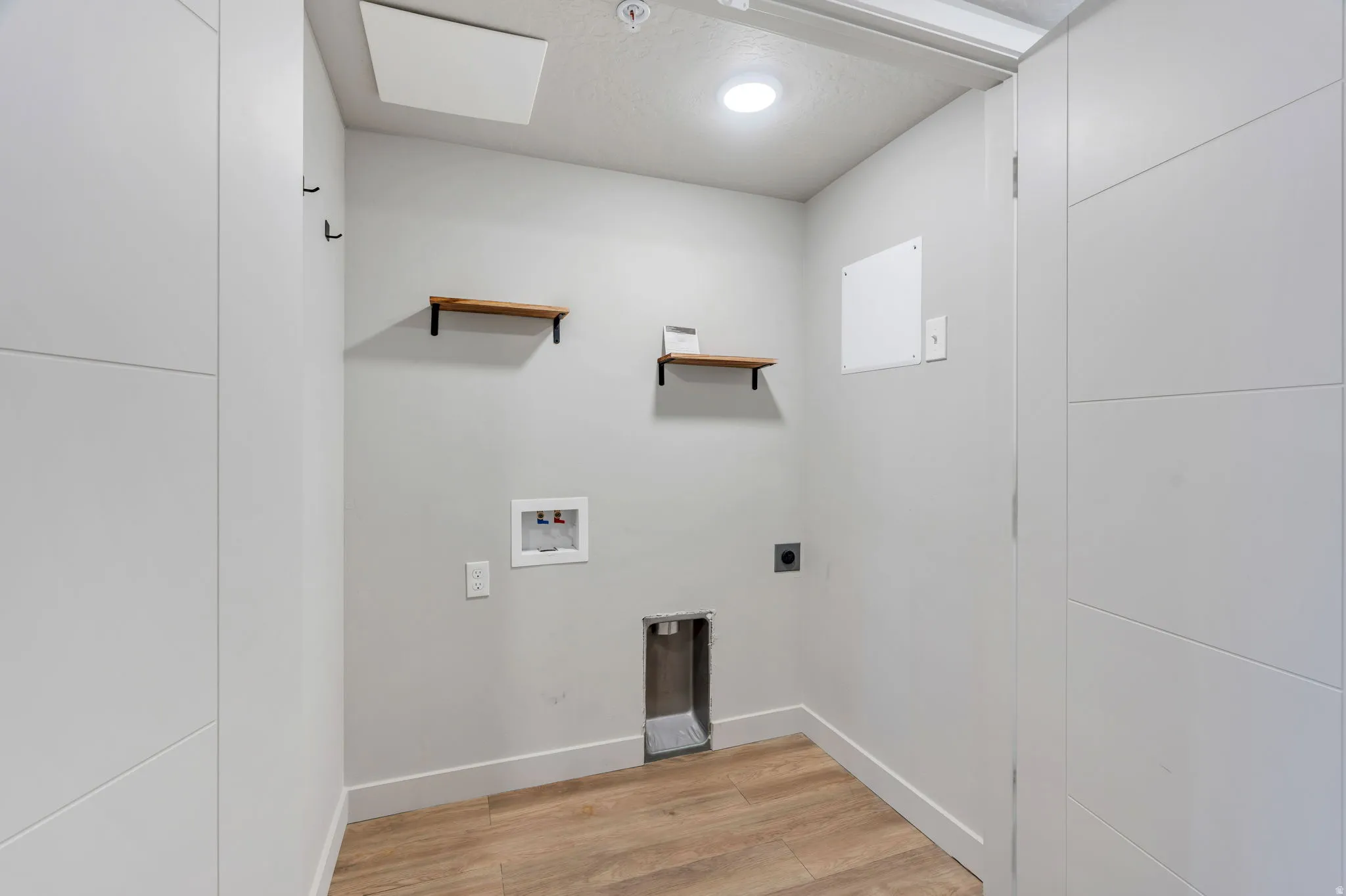 Dedicated laundry area with wood-finish flooring, two wall-mounted shelves, recessed lighting, and modern white trim