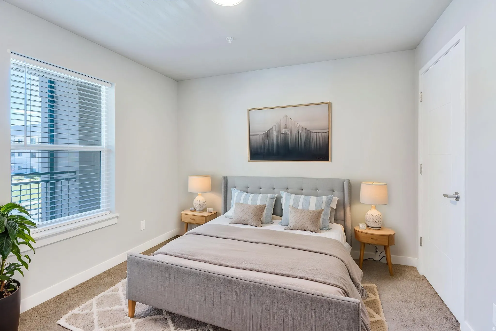Carpeted bedroom featuring a large window with blinds, a solid white door, and neutral wall tones