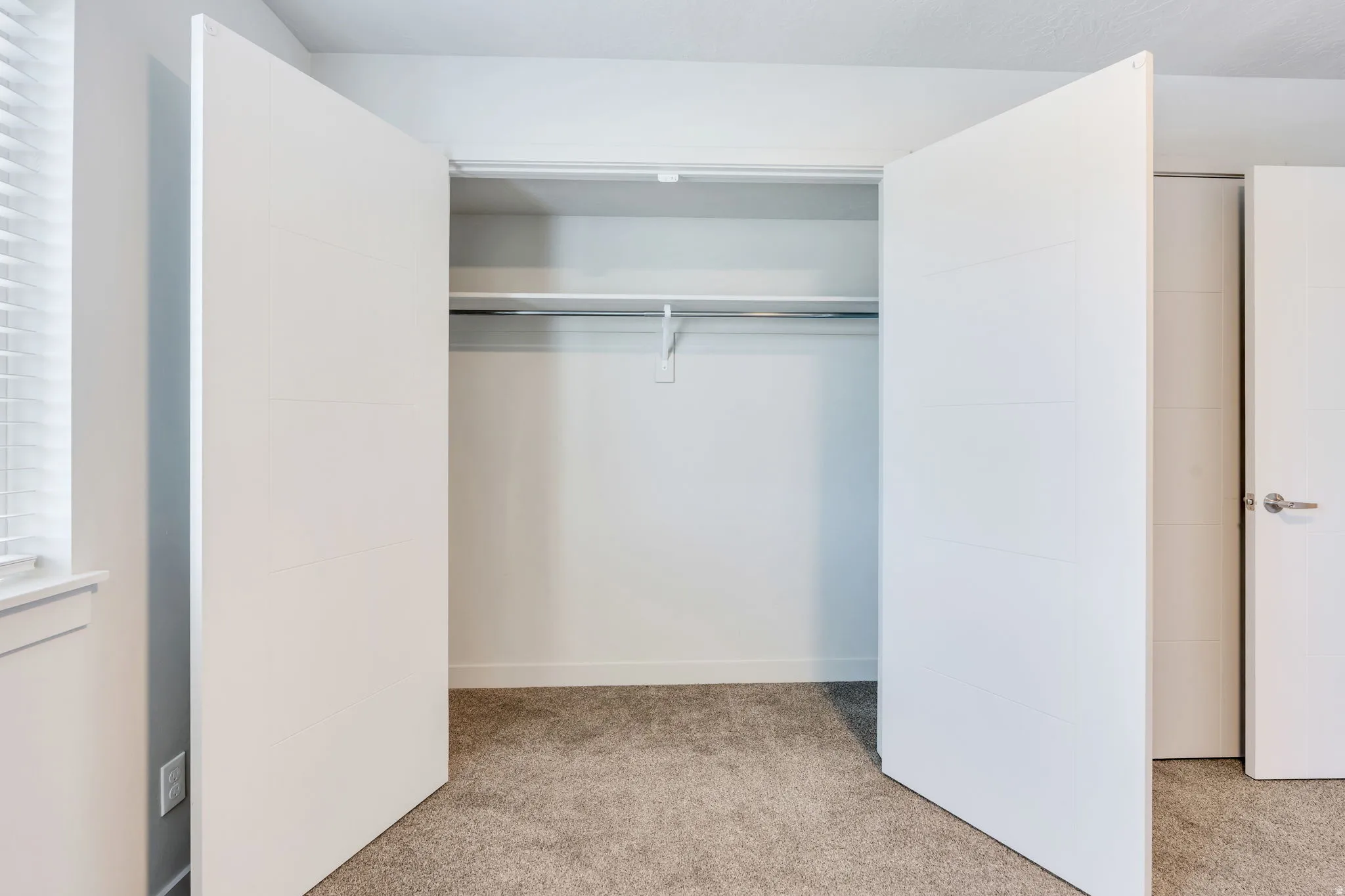 Spacious closet with white bifold doors, integrated shelving, and a chrome hanging rod