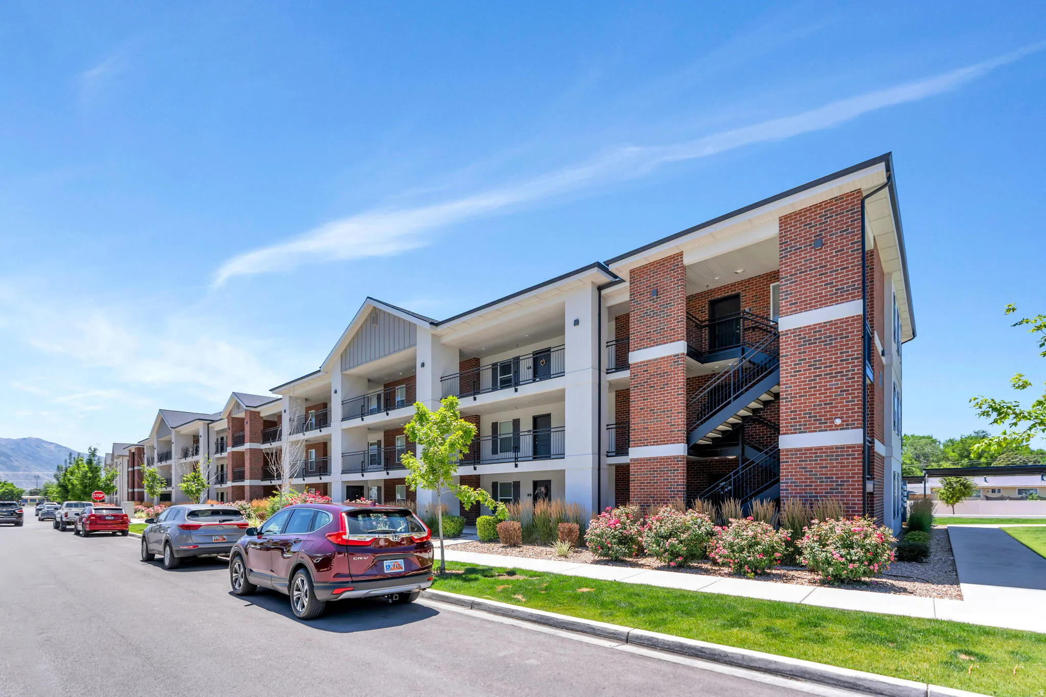 Contemporary apartment building featuring a brick and white siding exterior, private balconies, black metal railings, and exterior stairwells