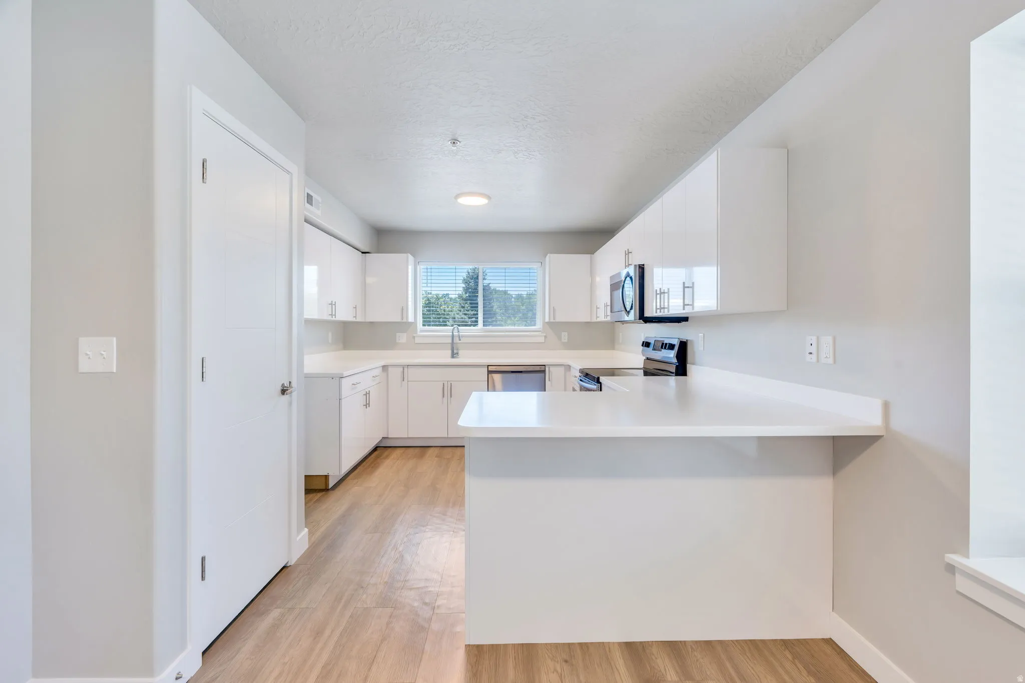 Modern kitchen featuring white cabinetry, light countertops, stainless steel sink, built-in microwave, and wood-finish flooring