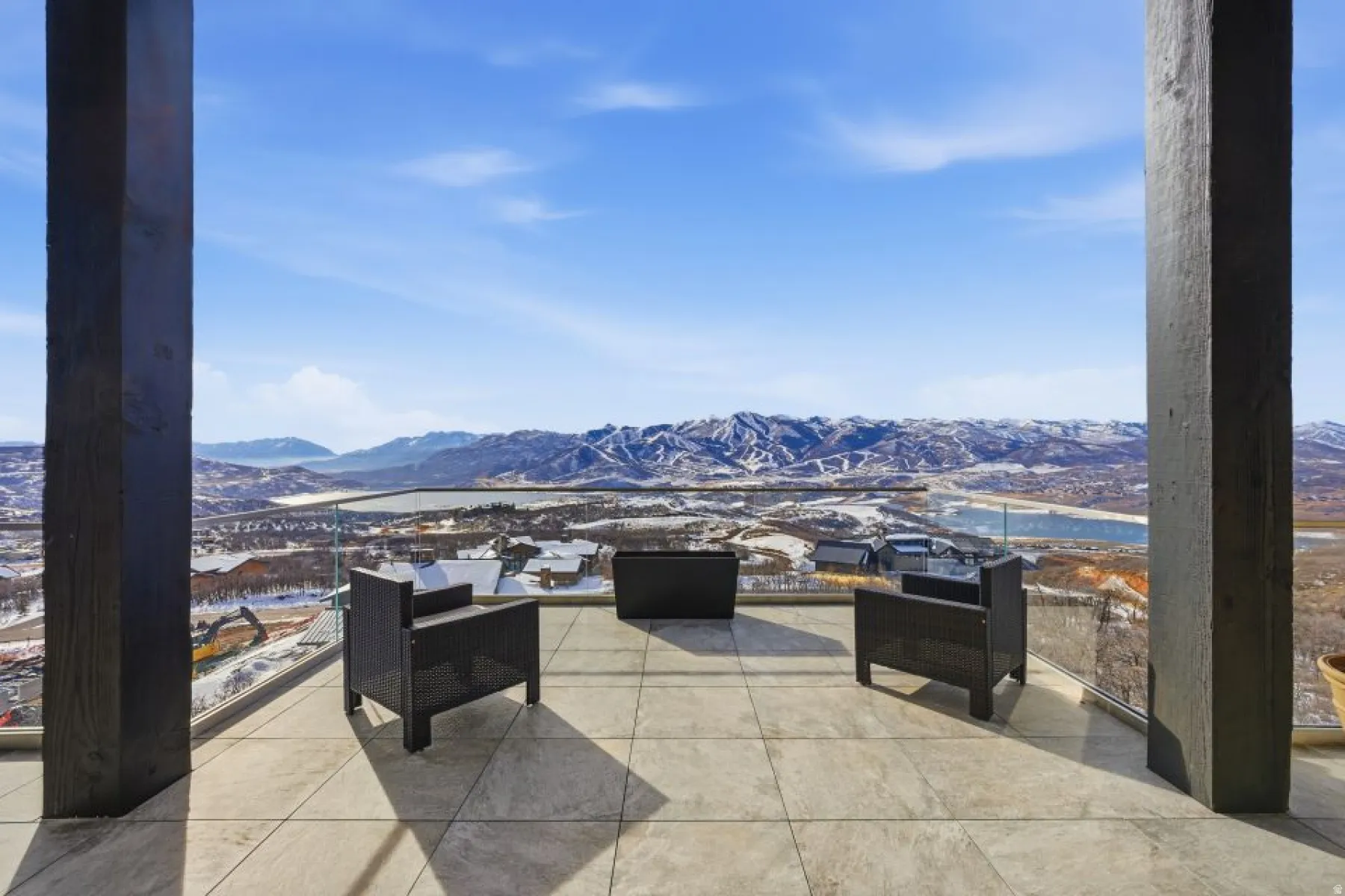 Expansive outdoor terrace featuring large format tile flooring, a glass railing system, and a mountain and lake backdrop
