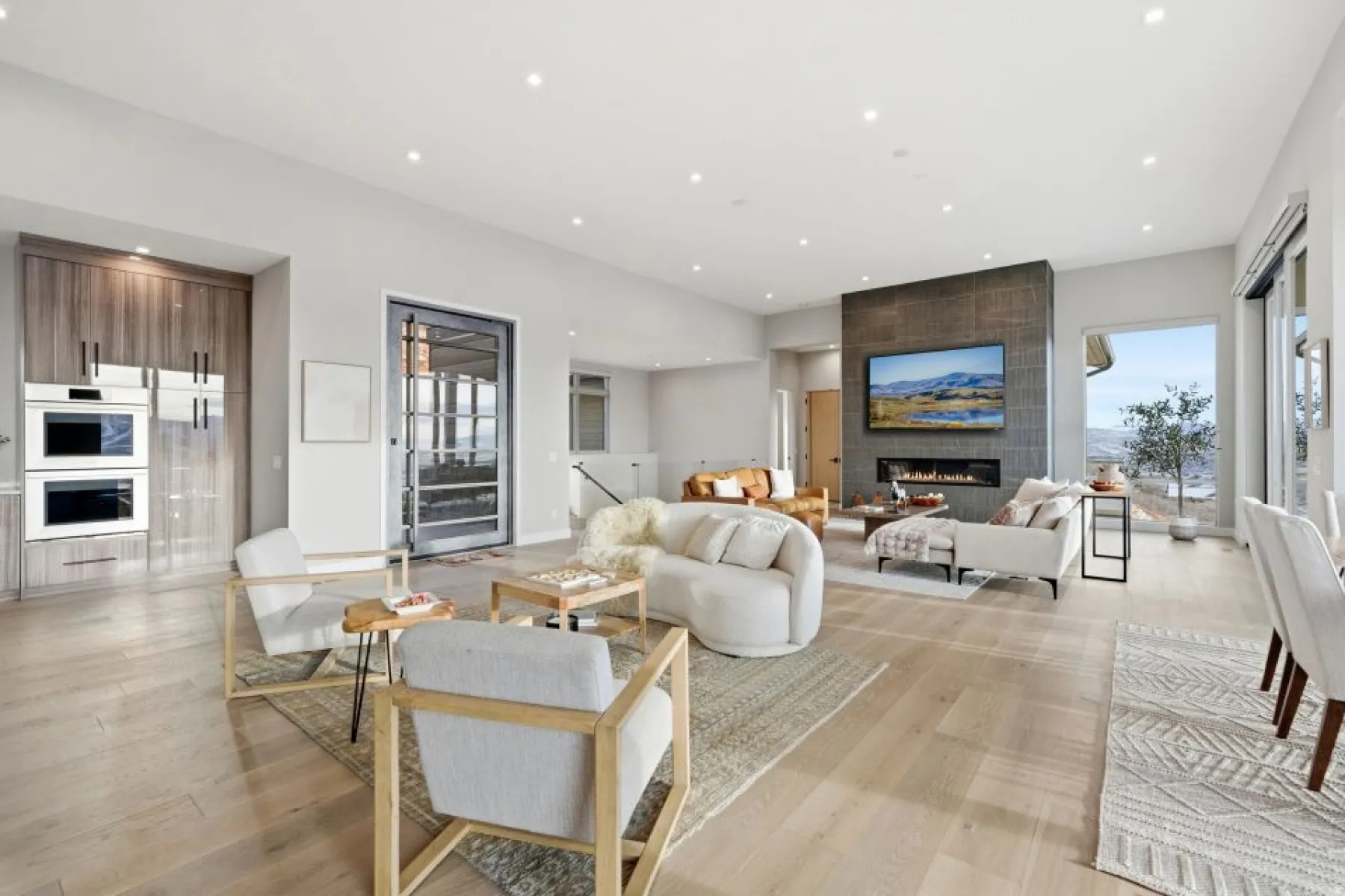 Spacious open-concept living area featuring light wood-finish flooring, recessed lighting, and a modern fireplace with a dark stone-tile surround