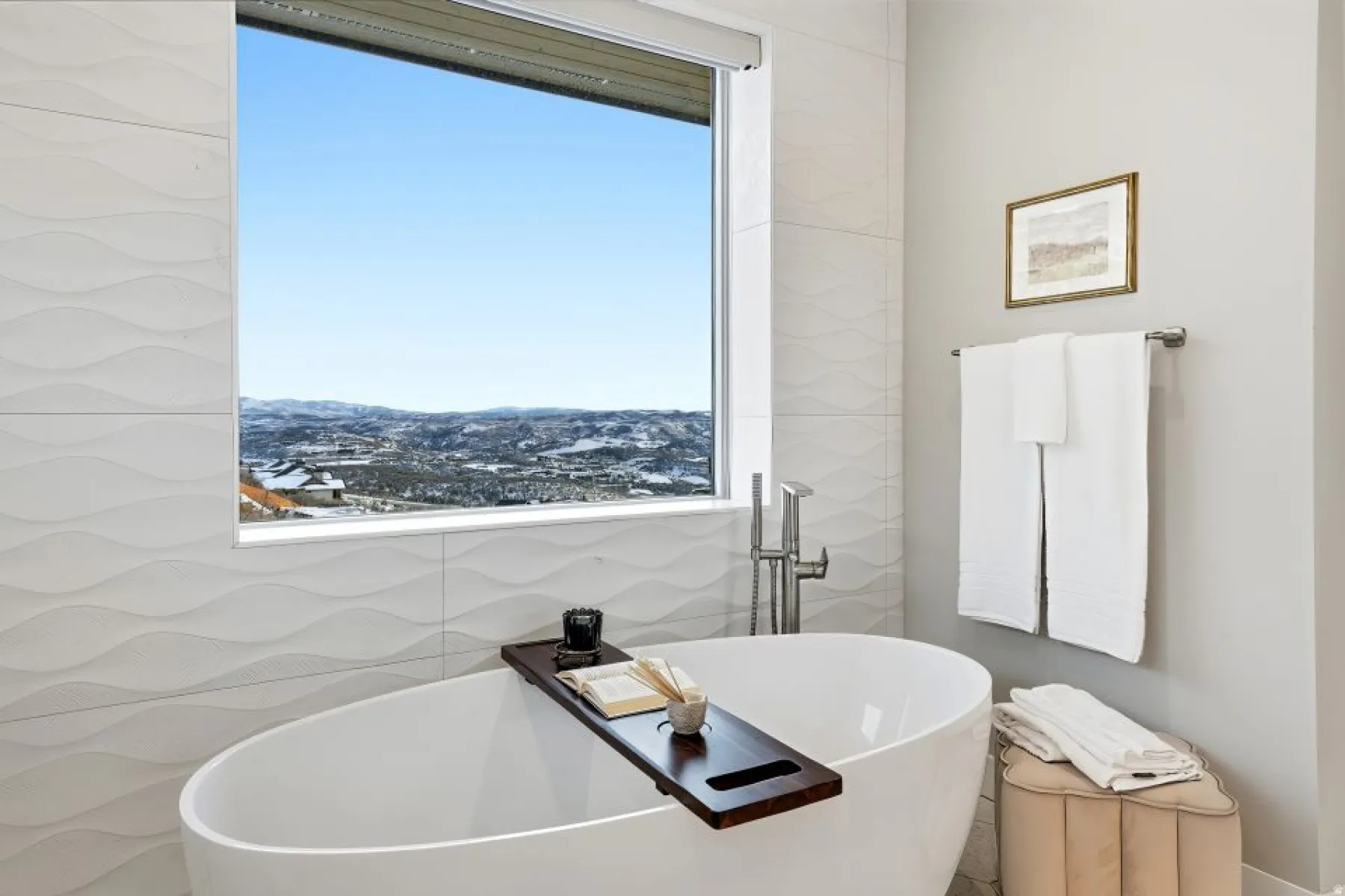 Freestanding oval soaking tub with floor-mounted brushed nickel faucet, set against a window with a mountain and city scenery