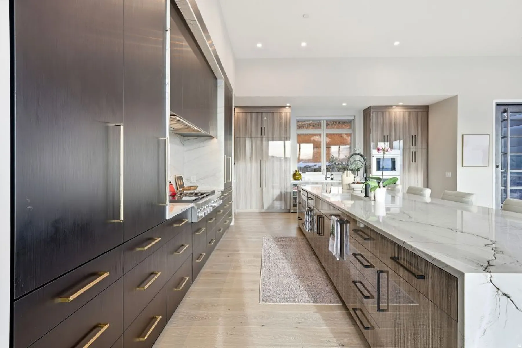 Spacious kitchen featuring an oversized center island with a waterfall countertop, light wood-finish flooring, and integrated stainless steel appliances