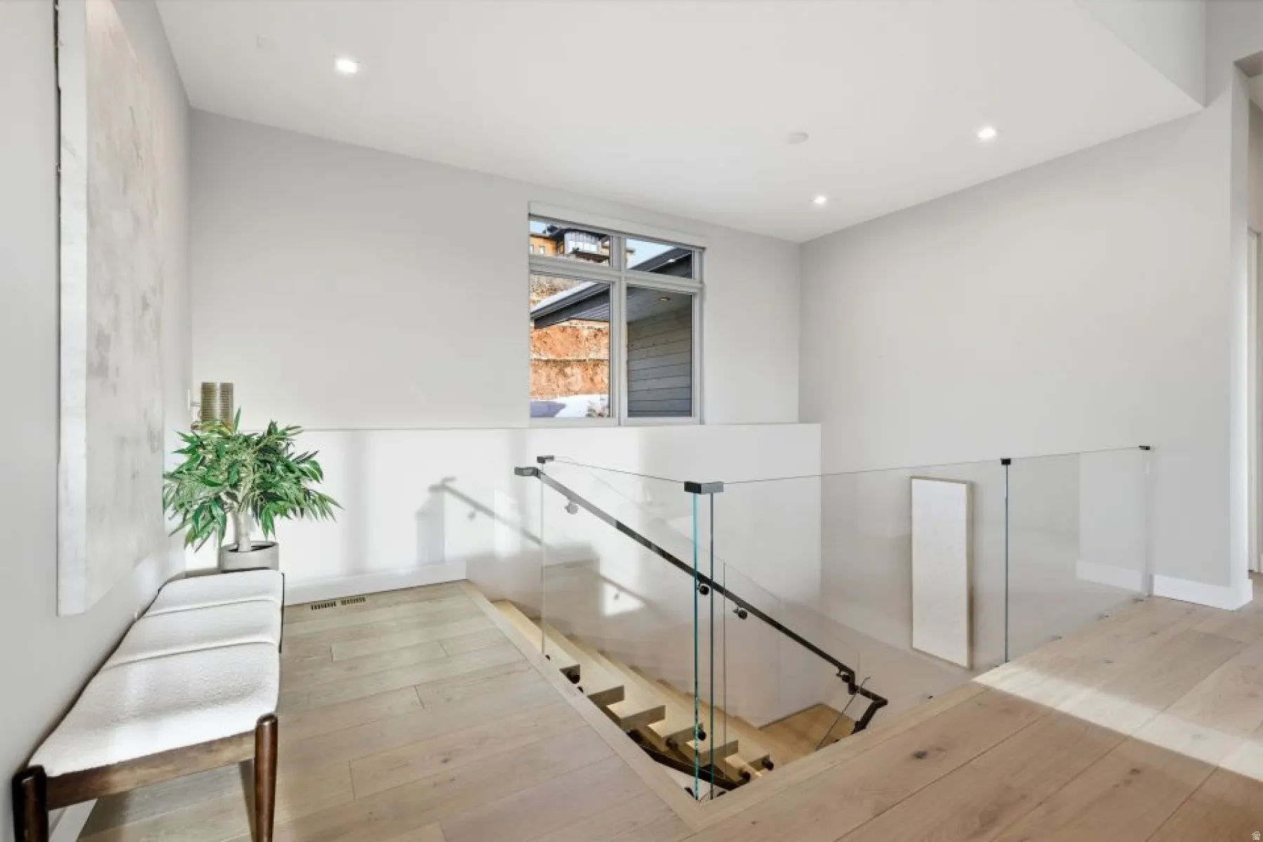 Upper landing featuring hardwood flooring and a modern glass panel railing system with a dark handrail