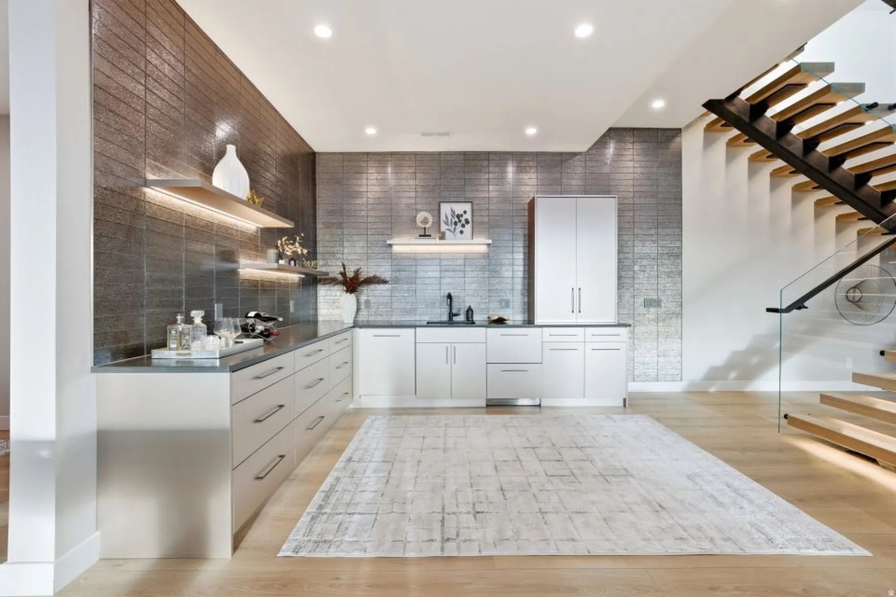 Contemporary wet bar area featuring a textured metallic-finish accent wall, white cabinetry, integrated sink, and recessed lighting