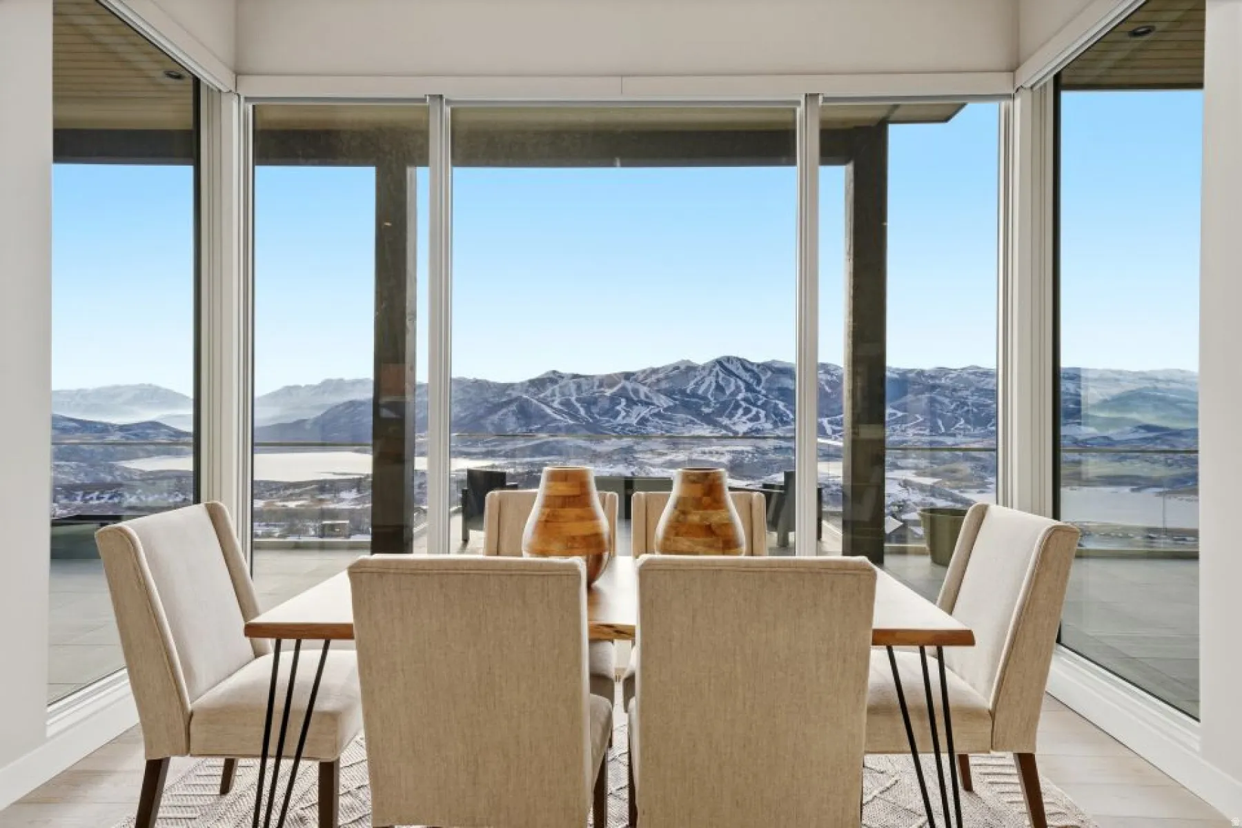 Dining area with expansive floor-to-ceiling windows, engineered wood flooring, and a panoramic mountain and lake backdrop