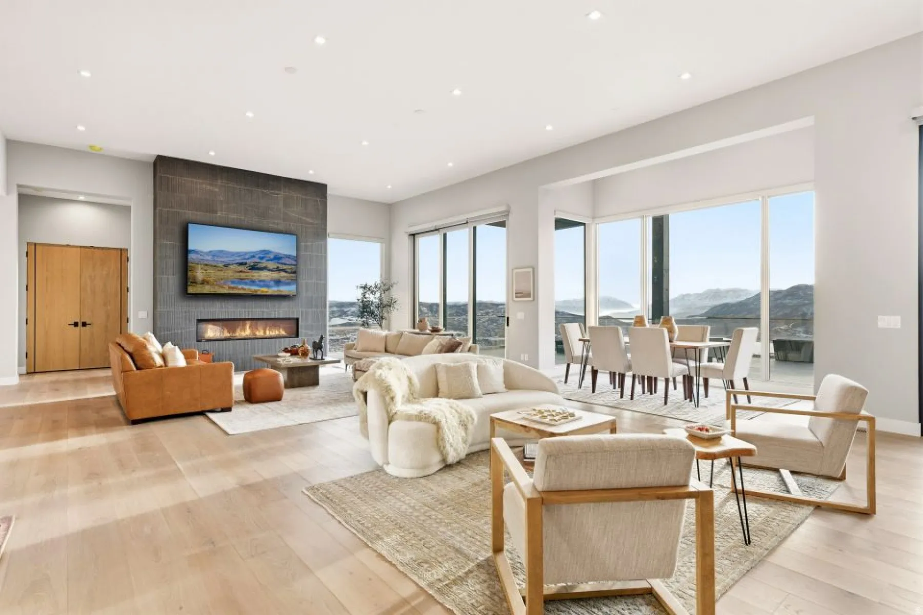 Expansive open-concept living area featuring light wood-finish flooring, a contemporary fireplace with a dark stone-clad surround, and large sliding glass doors