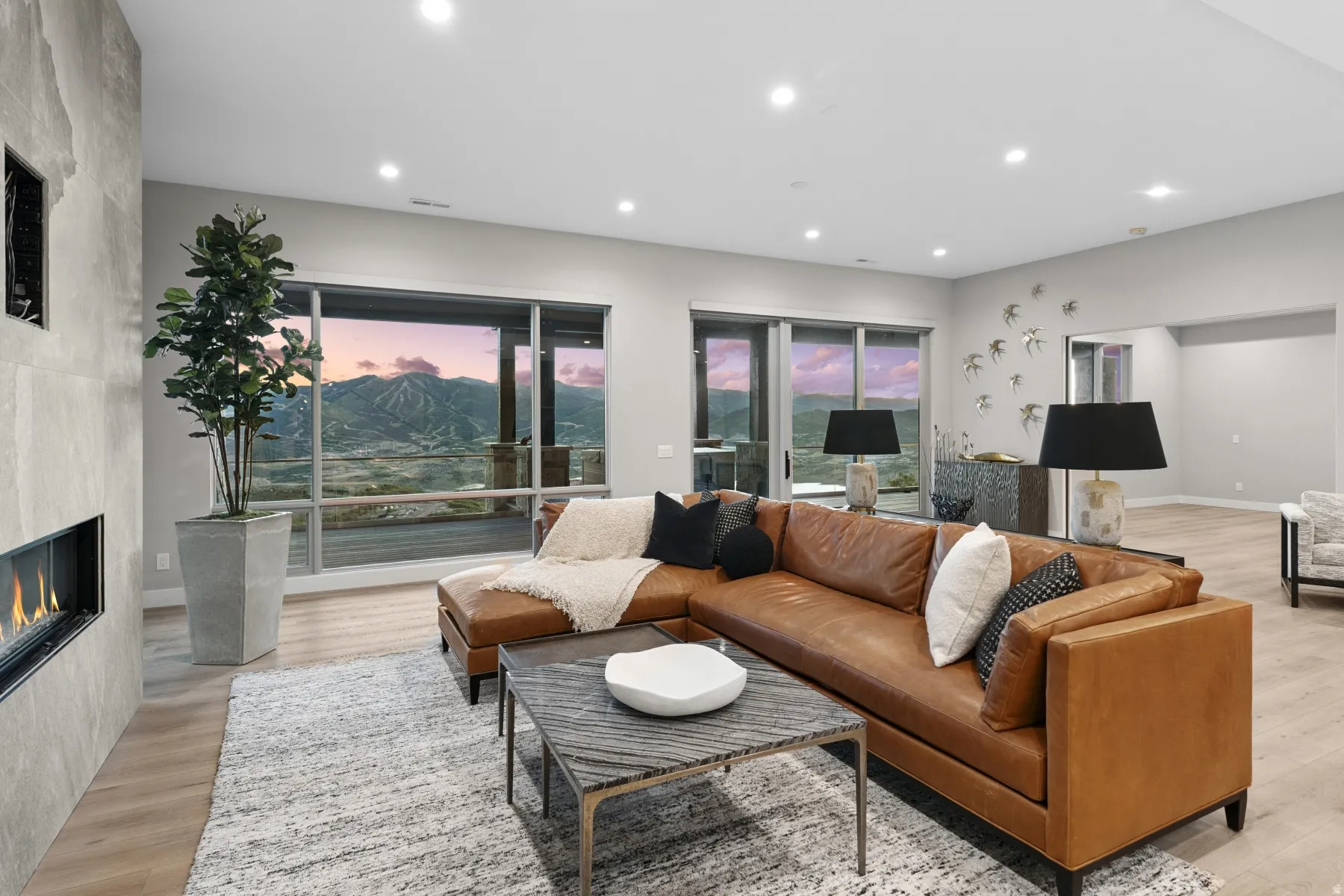 Spacious living area featuring large windows showcasing mountain scenery, a linear fireplace with a stone surround, recessed lighting, and wood-finish flooring