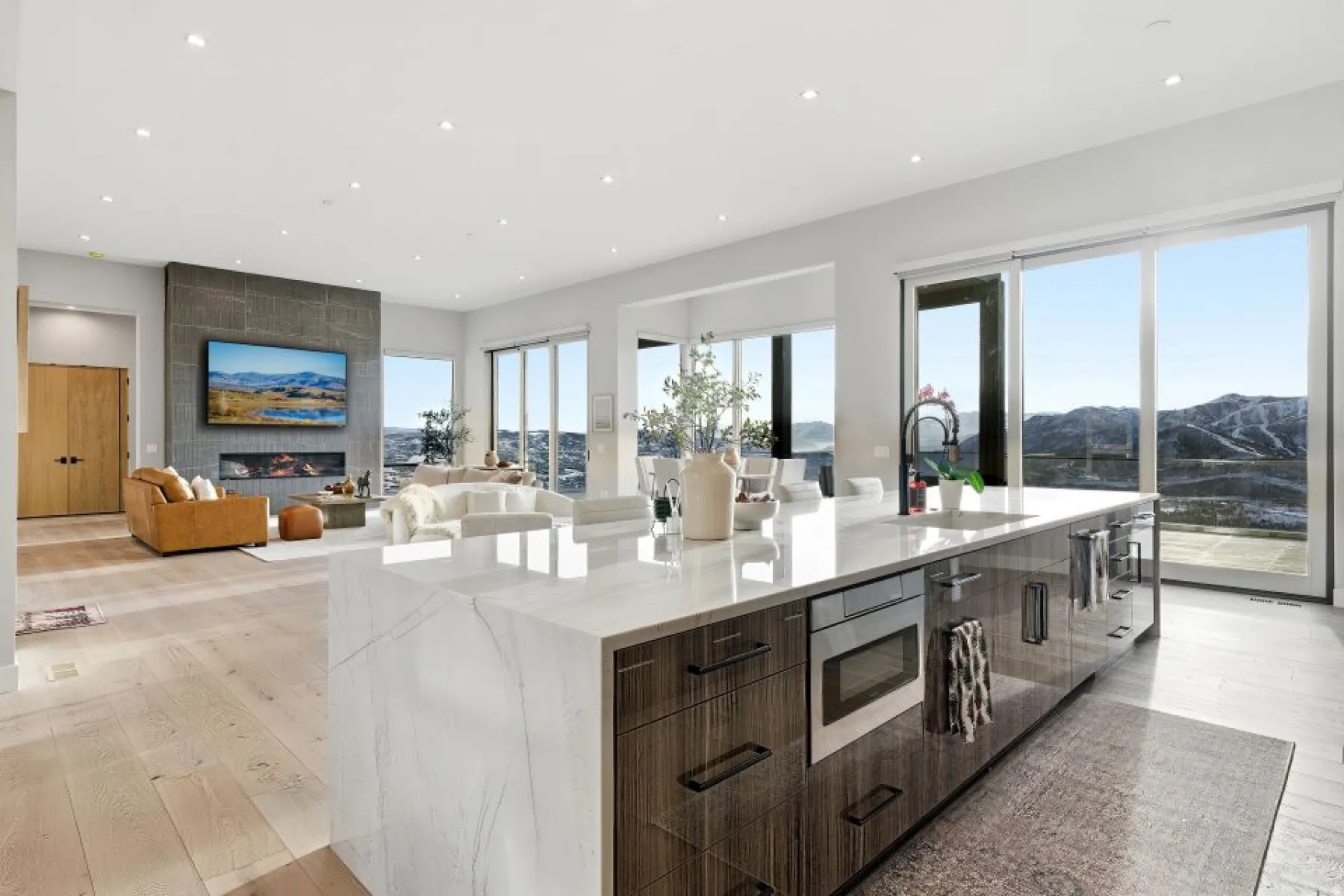 Open-concept living space with light wood-finish flooring, a contemporary kitchen island featuring a waterfall-edge countertop, and dark wood cabinetry