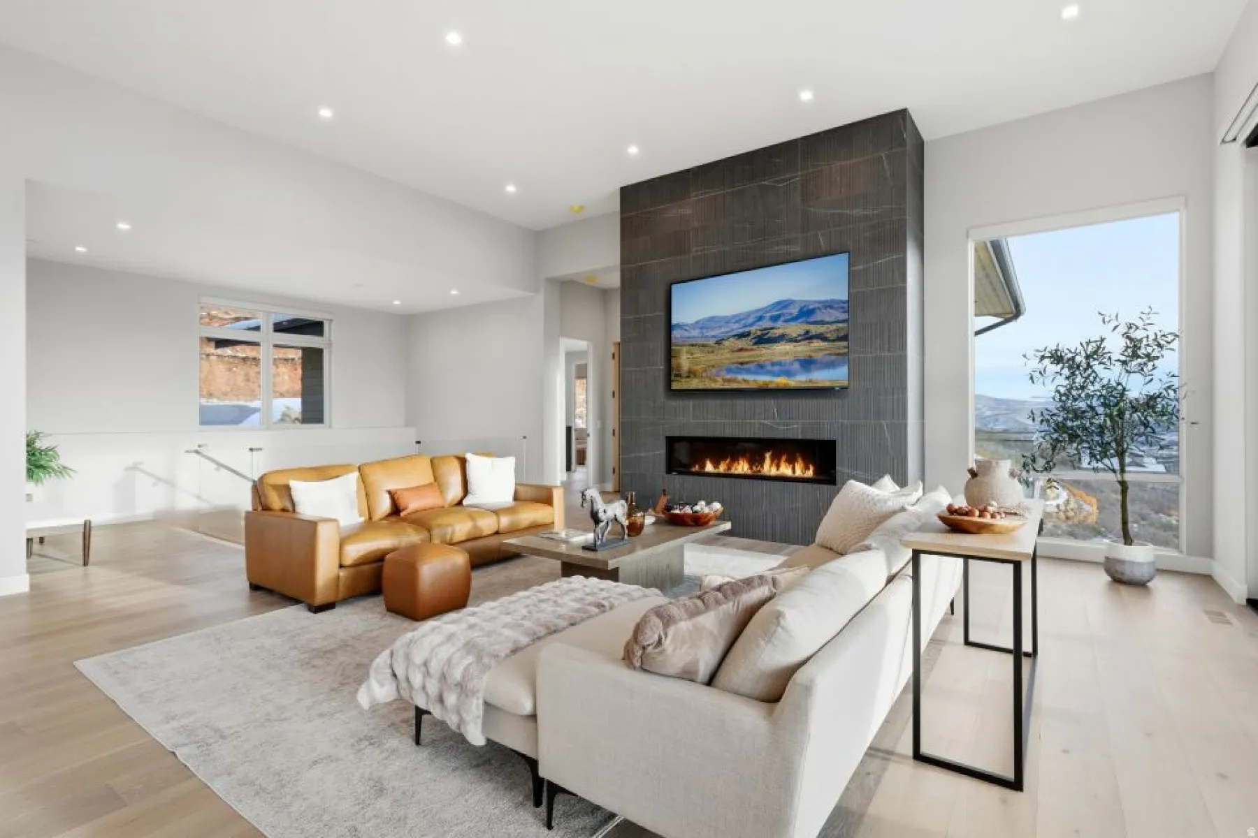 Spacious living area featuring a linear fireplace set within a dark tile accent wall, recessed lighting, expansive window with outdoor scenery, and light wood-finish flooring