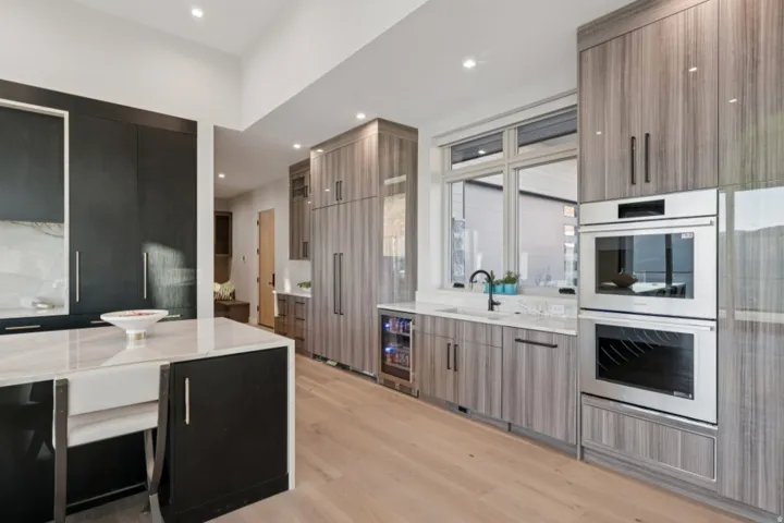 Gourmet kitchen featuring light wood-finish flooring, a central island with a farmhouse sink, integrated stainless steel appliances, a beverage refrigerator, and light wood-finish cabinetry