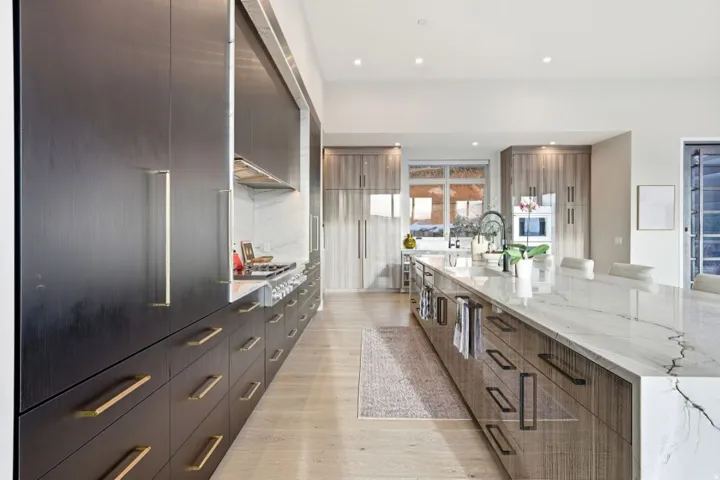 Spacious kitchen featuring an oversized center island with a waterfall countertop, light wood-finish flooring, and integrated stainless steel appliances