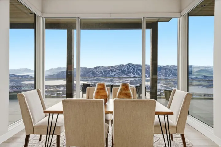 Dining area with expansive floor-to-ceiling windows, engineered wood flooring, and a panoramic mountain and lake backdrop