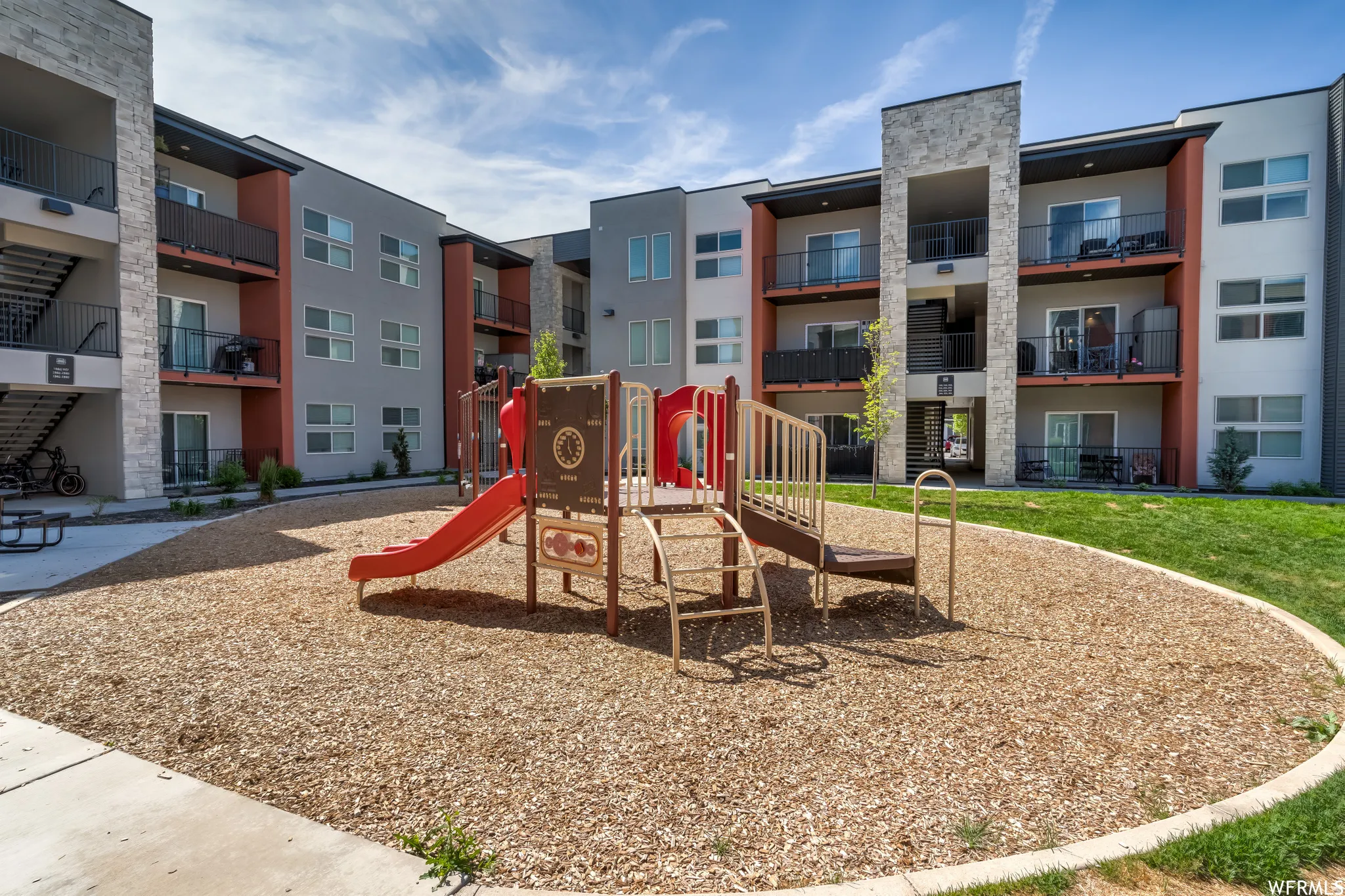 Community playground area with wood chip surfacing, green lawn border, and a concrete pathway