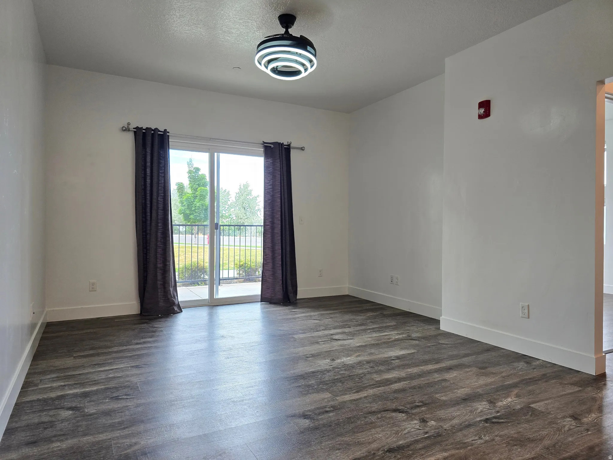 Spacious room featuring wood-finish flooring, white walls, and a contemporary ceiling light fixture