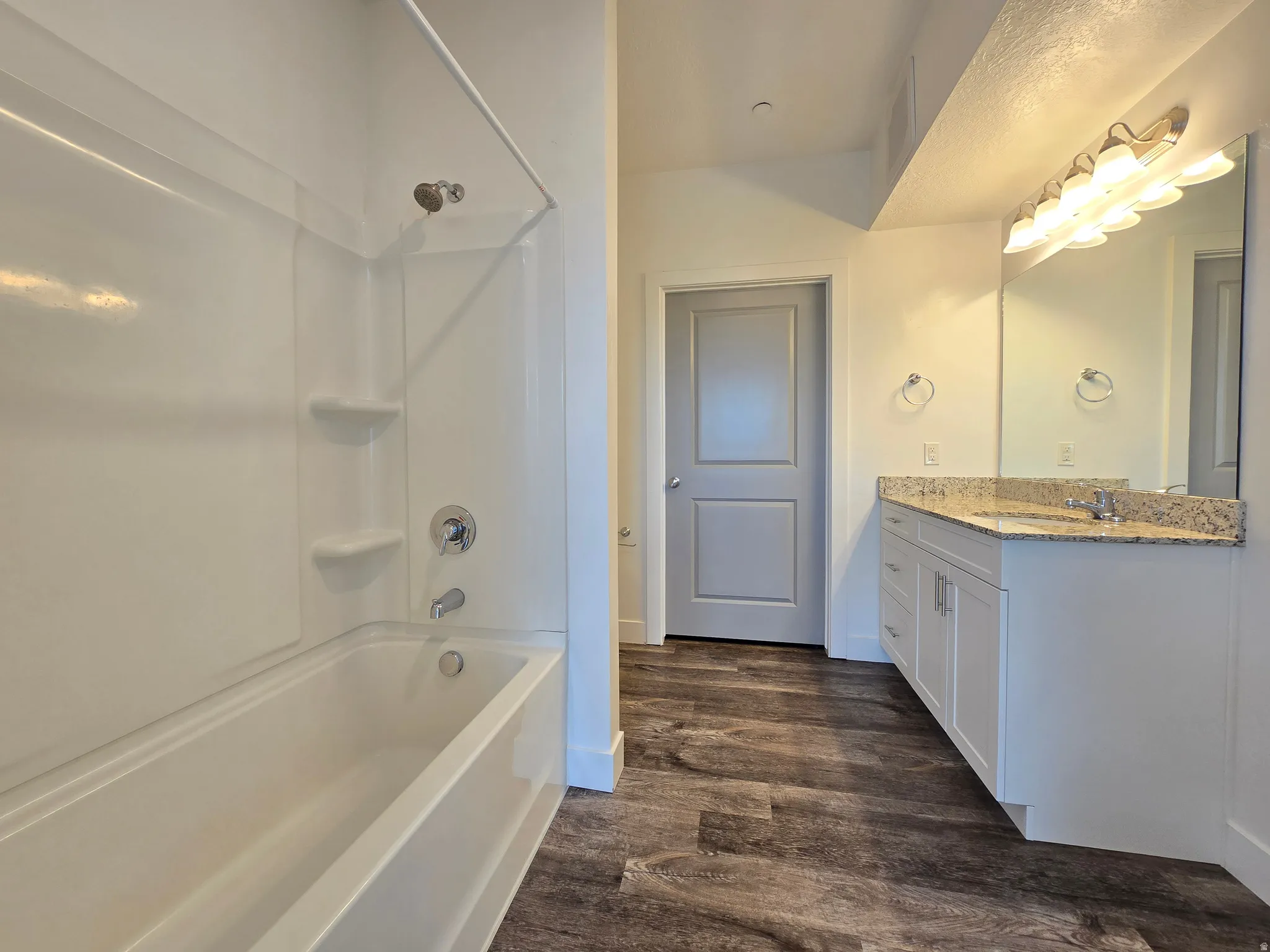 Full bathroom featuring a white tub and shower combination with chrome fixtures, a light-colored vanity with a granite-style countertop, an integrated sink, and a large mirror with multi-bulb lighting