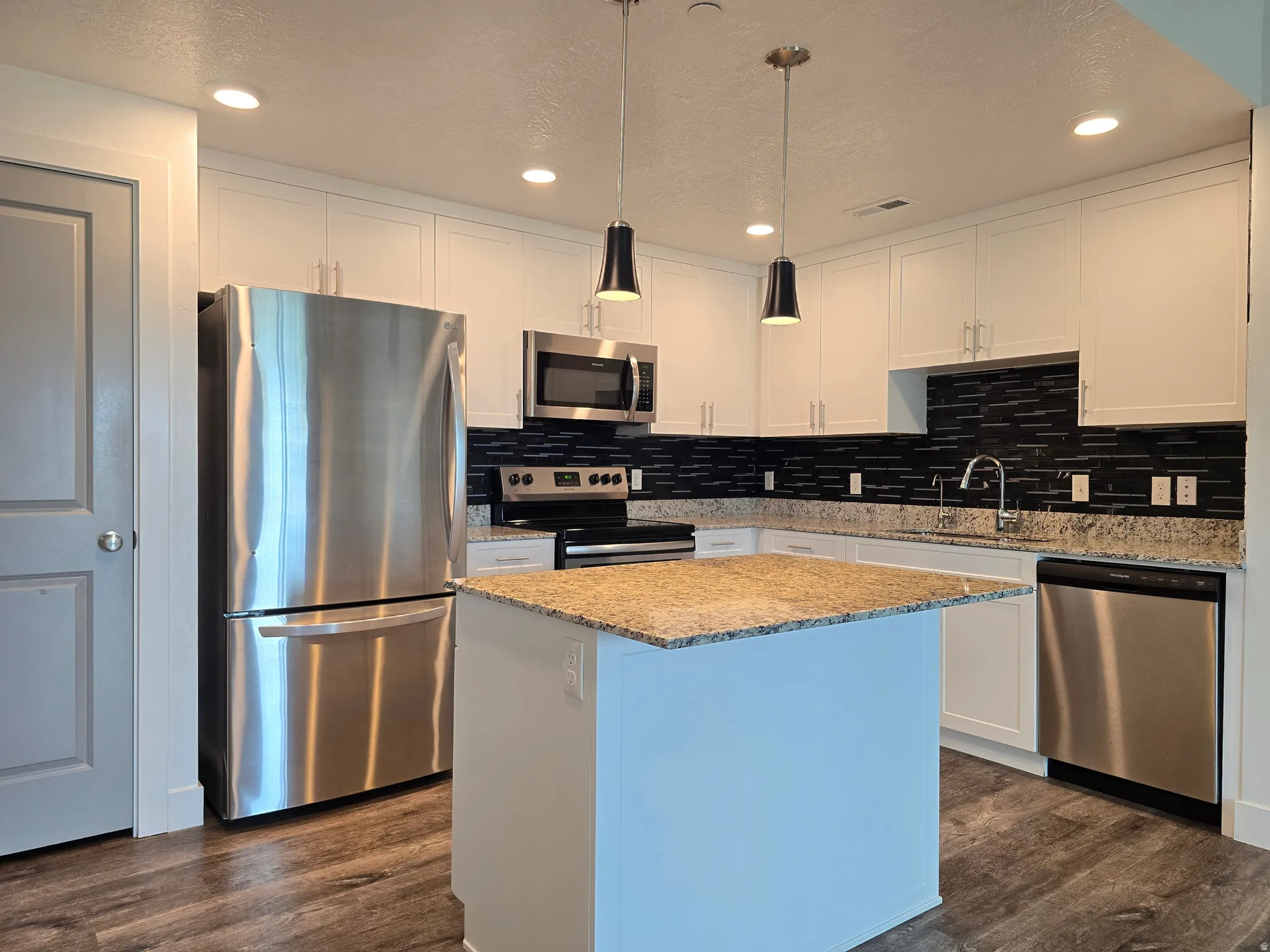 Modern kitchen featuring a central island with granite countertop, white cabinetry, and stainless steel appliances