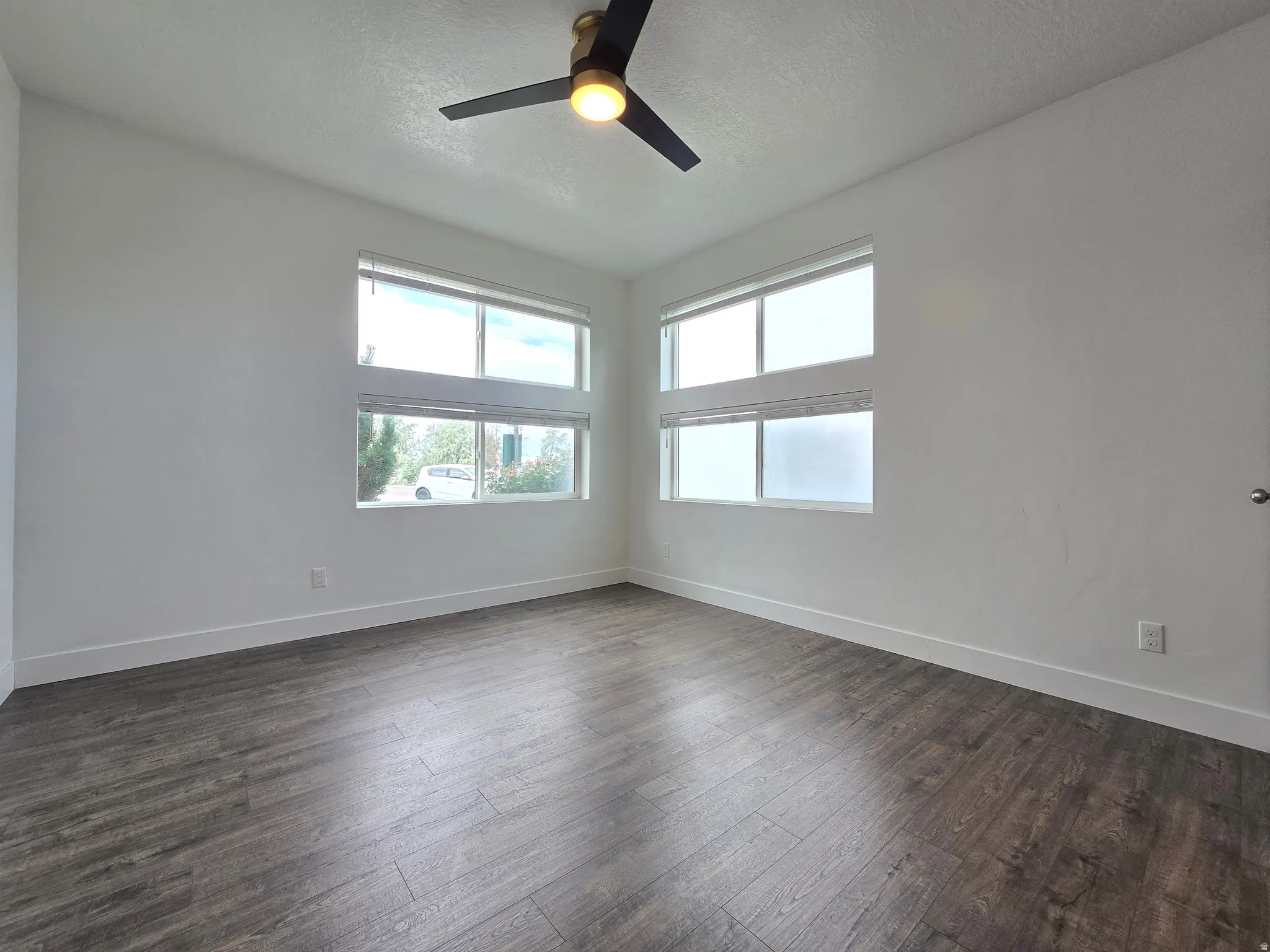 Spacious room featuring wood-finish flooring, white baseboards, and a modern ceiling fan