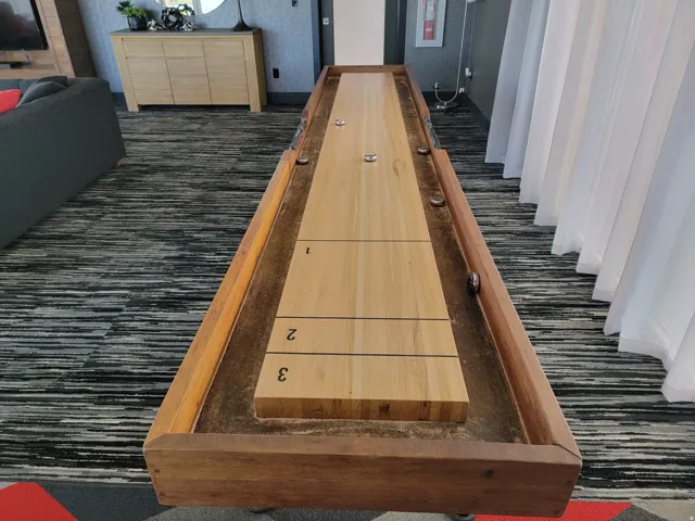 Shuffleboard table featuring a light wood playing surface and dark wood trim