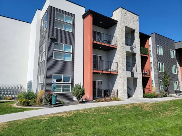 Contemporary multi-story facade featuring stone accents, private balconies with black railings, and a mix of white, red-orange, and dark gray siding