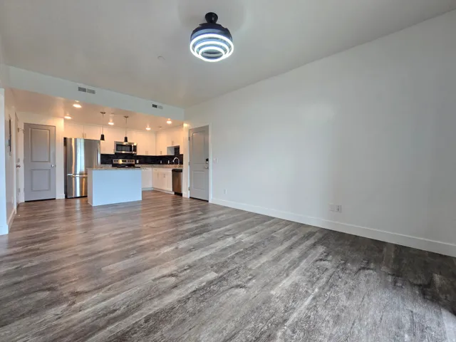 Open-concept living area featuring wood-finish flooring, a contemporary ceiling light fixture, and a kitchen with white cabinetry, stainless steel appliances, and an island