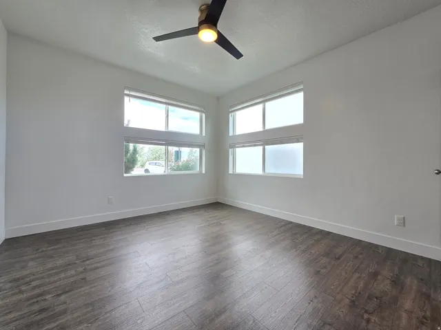 Spacious room featuring wood-finish flooring, white baseboards, and a modern ceiling fan