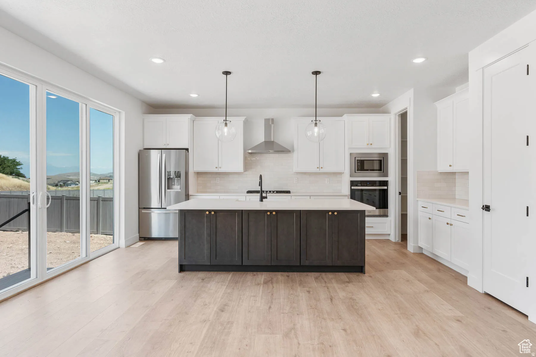 Contemporary kitchen featuring a dark-toned island with a light-toned countertop, white cabinetry, stainless steel appliances, and wood-finish flooring