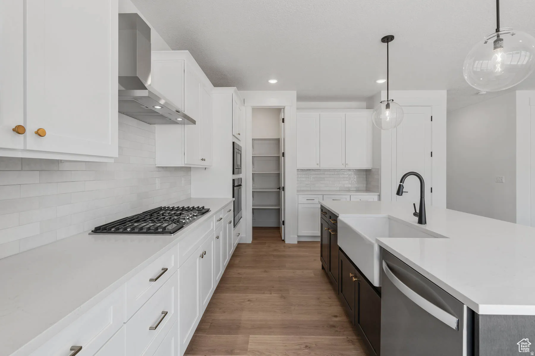 Modern kitchen featuring white cabinetry, light wood-finish flooring, and a gas cooktop with stainless steel hood