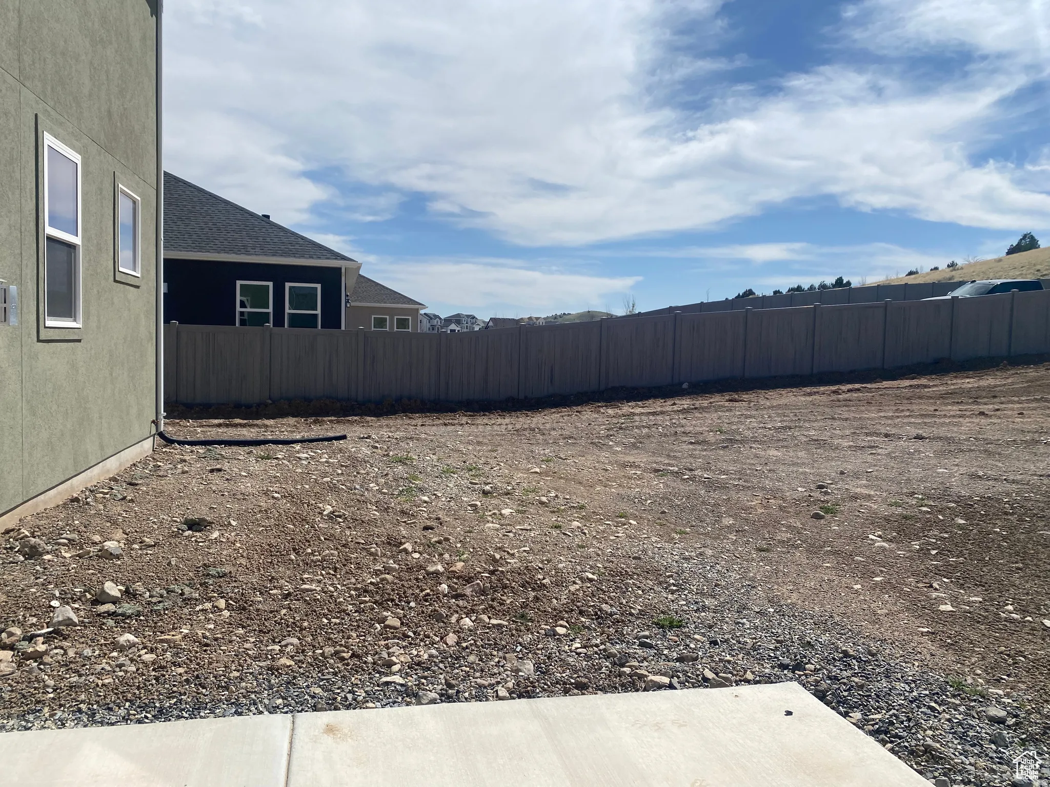 Expansive undeveloped lot featuring a privacy fence, concrete patio, and a natural, rocky landscape